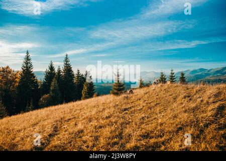 Eine schöne horizontale Aufnahme der aufgehenden Sonne und hohen Berge unter dem wolkigen Himmel Stockfoto