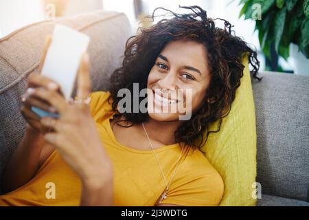 Pläne zuerst ... dann will ich von diesem Sofa steigen. Hochwinkelporträt einer attraktiven jungen Frau, die ihr Handy benutzt, während sie sich am Wochenende zu Hause entspannt. Stockfoto