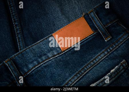 Lederfarbenes, braunes Lederlabel, das auf eine blaue Denim-Jeans genäht wurde. Angedeuteter Jeans-Anhänger Stockfoto