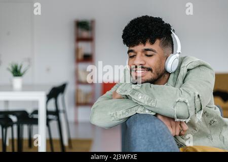 Glücklicher, multirassischer Mann, der auf dem Sofa liegt und Musik über Kopfhörer hört Stockfoto