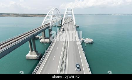 Luftaufnahme entlang der langen schönen Brücke über dem türkisfarbenen Meer. Aktion. Fliegen über die Biegebrücke mit fahrenden Autos. Stockfoto