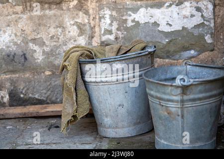 Zwei alte Metall-Reinigungseimer stehen an einer Wand Stockfoto