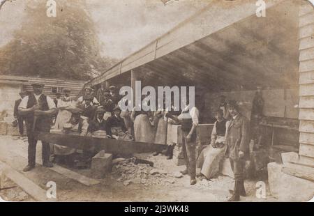 Foto von Steinmetzen in einem Hof, Anfang 20. Jahrhundert. Zwei Männer schneiden mit einer Frig-bob-Säge einen Steinblock, die anderen Männer stehen dahinter herum. Im Hintergrund sind Werkzeuge und Blöcke aus bearbeiteten Steinen zu sehen Stockfoto