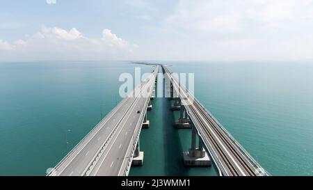 Luftaufnahme entlang der langen schönen Brücke über dem türkisfarbenen Meer. Aktion. Fliegen über die Biegebrücke mit fahrenden Autos. Stockfoto