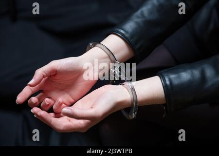 Festnahme, fesselte Hände einer kriminellen Frau aus nächster Nähe. Vorne verschlossene Handschellen, Schutz vor Verbrechen und Gesetzesverstößen. Stockfoto