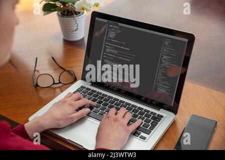 Computercode, Softwarekonzept. Programmierer, die mit einem Laptop arbeiten, Programmiercode auf dem Bildschirm, Bürohintergrund. Entwicklung von Codierungstechnologien. Stockfoto