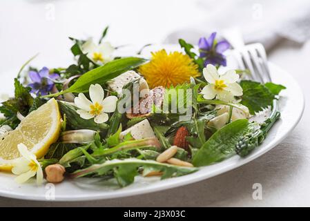 Frühlingssalat mit Dandelion, Spargel, Bärlauch, Blumen, Brennnessel und Frischkäse. Gesunde Frühlingsnahrungsmittelzutaten. Stockfoto