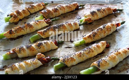 Frisch gebackener Spargel, eingewickelt in Prosciutto und Blätterteig, verziert mit Mohnsamen auf Holzboden. Frühjahrssaison. Direkt darüber. Stockfoto