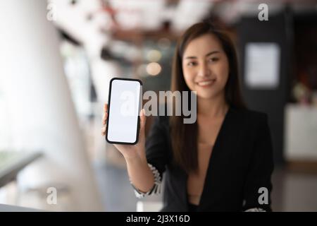 Mockup Bild von einer schönen Geschäft asiatische Frau zeigt Handy mit weißen Bildschirm leer Stockfoto