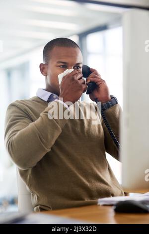 Einen Termin für seinen hausarzt vereinbaren. Aufnahme eines jungen Geschäftsmannes, der seine Nase an seinen Schreibtisch bläst. Stockfoto
