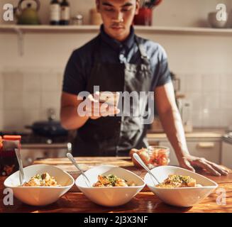 Die kulinarische WIZ schlägt wieder zu. Aufnahme eines jungen Mannes mit einem Smartphone, um Fotos von einer gesunden Mahlzeit zu machen, die er zu Hause zubereitet hat. Stockfoto