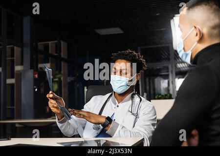 Afrikanischer Arzt zeigen Röntgen asiatischen Patienten. Schwarzer Chirurg Analyse Röntgen und Diagnose Patient in der medizinischen Klinik Stockfoto