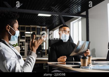Ein asiatischer Patient konsultiert einen Arzt des schwarzen Chirurgen und diskutiert das Röntgenbild. Vorbereitung auf den Betrieb. Afrikanischer Arzt, der einen Patienten untersucht Stockfoto