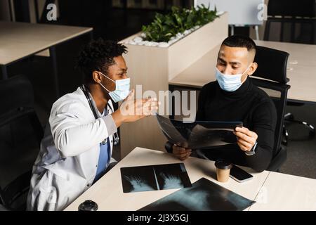 Afrikanischer Arzt zeigen Röntgen asiatischen Patienten. Schwarzer Chirurg Analyse Röntgen und Diagnose Patient in der medizinischen Klinik Stockfoto