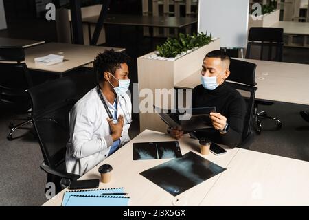 Afrikanischer Arzt zeigen Röntgen asiatischen Patienten. Schwarzer Chirurg Analyse Röntgen und Diagnose Patient in der medizinischen Klinik Stockfoto