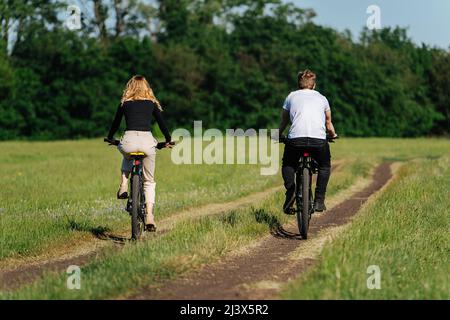 Pärchen, die auf dem Land mit dem Fahrrad unterwegs sind. Blick von hinten. Reiten auf der Strecke entlang der Baumgrenze. Stockfoto