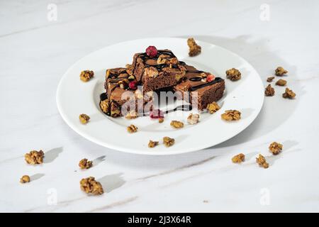 Schokoladen-Brownie-Quadrate mit Walnussstücken, Schokoladenfäden und Müsli. Natürliches, gesundes Lebensmittelkonzept. Hohe Ansicht. Stockfoto
