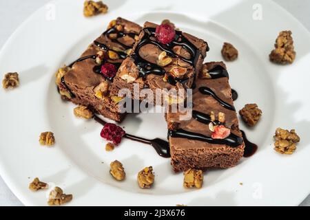 Schokoladen-Brownie-Quadrate mit Walnussstücken, Schokoladenfäden und Müsli. Natürliches, gesundes Lebensmittelkonzept. Hohe Ansicht. Stockfoto