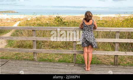 Blonde Frau auf Holzsteg oder Brücke mit fließenden Kleid vom Wind bewegt und modisch im Meer Stockfoto