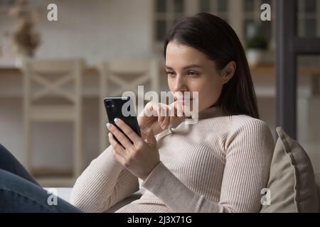 Fokussierte tausendjährige Frau, die zu Hause ein Mobiltelefon verwendet Stockfoto