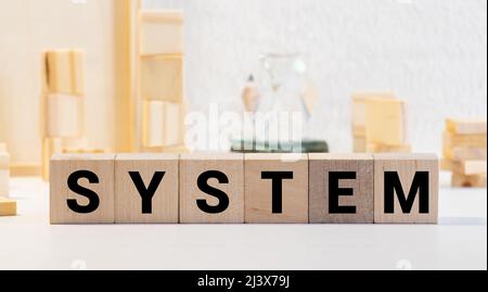 System - Wort aus Bausteinen. Auf einer schwarzen Tastatur befindet sich eine Reihe von Holzwürfeln mit einem Wort in schwarzer Schrift. Stockfoto