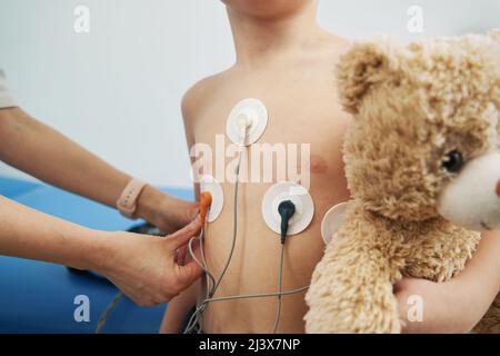 Kinderarzt überprüft den Herzrhythmus des Kindes mit dem EKG-holter-Monitor Stockfoto