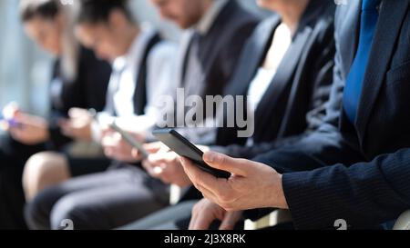Eine Gruppe von unkenntlichen Kandidaten, die auf ein Vorstellungsgespräch warten und drahtlose Technologien in einem Flur einsetzen Stockfoto