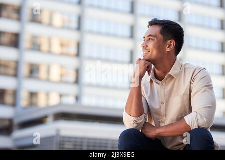 Ein junger asiatischer Geschäftsmann sitzt und blickt lächelnd über die Stadt Stockfoto