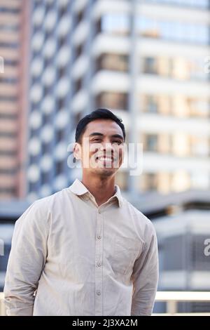 Ein junger, attraktiver asiatischer Mann steht vor Stadtgebäuden Stockfoto