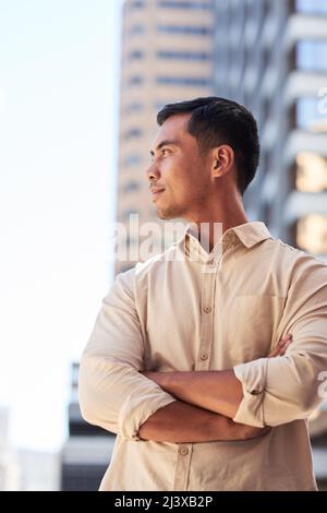 Ein junger, attraktiver asiatischer Mann blickt mit gekreuzten Armen über die Stadt Stockfoto