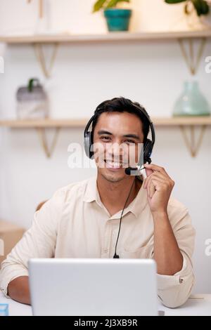 Ein junger asiatischer Mann hält das Mikrofon seines Headsets und lächelt die Kamera an Stockfoto