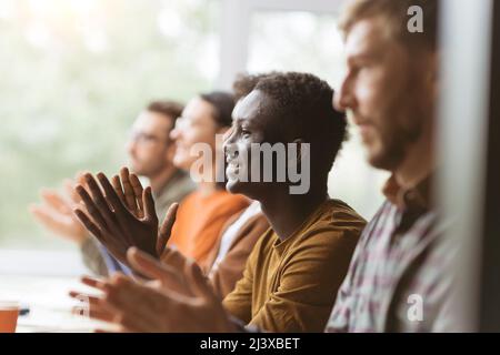 Eine Gruppe zufriedener Mitarbeiter applaudiert, während sie an derselben Ta sitzen Stockfoto