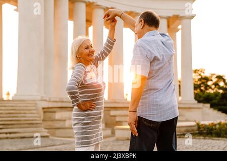 Weißes Seniorenpaar tanzt und lächelt gemeinsam im Freien bei Sonnenuntergang Stockfoto