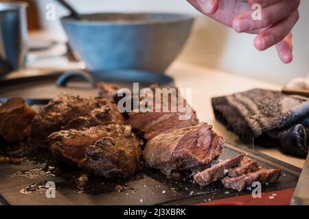 Salz, das auf geschmorte Rinderbacken fällt, gekocht in Rotweinsauce auf Schneidebrett. Langsam gekochter Fleischeintopf. Stockfoto