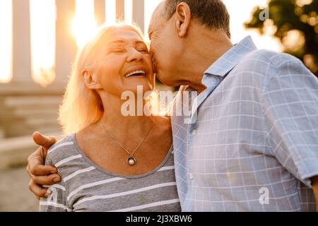 Weißes Seniorenpaar küsst und lacht gemeinsam im Freien bei Sonnenuntergang Stockfoto