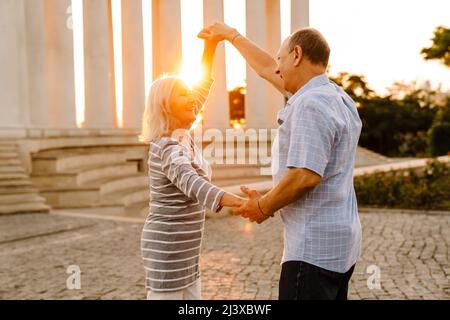 Weißes Seniorenpaar tanzt und lächelt gemeinsam im Freien bei Sonnenuntergang Stockfoto
