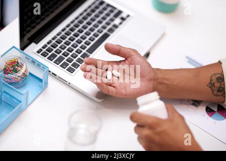 Eine Nahaufnahme von Kopfschmerzen oder Grippepillen in einer mans-Hand an seinem Schreibtisch im Büro Stockfoto