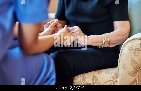 Sie sind jetzt in sicheren Händen. Ausgeschnittene Aufnahme einer Krankenschwester, die eine ältere Frau in den Händen hält. Stockfoto