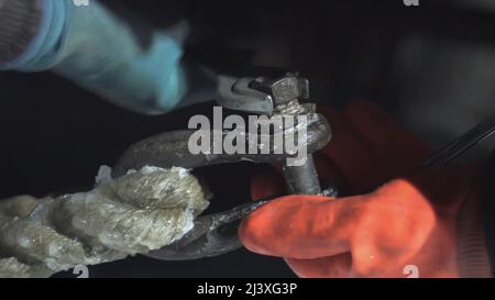 Ziehen Sie die Schraube mit den Händen aus der Nähe an. CLIP. Herrenhände in orangefarbenen Handschuhen an Bord des Schiffes ziehen die Schraube aus der Verankerung des Schiffes nachts fest Stockfoto