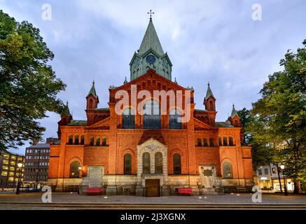 Rote Backsteinfassade der Caroli-Kirche, Uhr auf dem Turm am Abend, Malmö, Schweden. Stockfoto