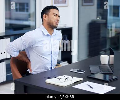 Die Folgen einer schlechten Körperhaltung. Aufnahme eines Geschäftsmannes, der bei der Arbeit unter Rückenschmerzen leidet. Stockfoto