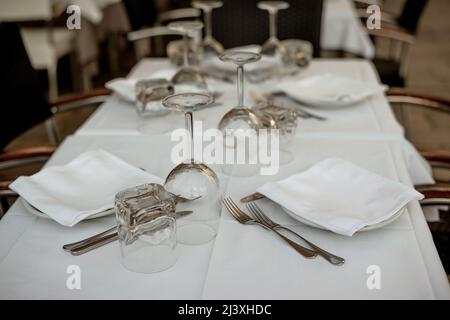 Wunderschöne Tischeinstellung. Leere Gläser, Besteck und Servietten auf einem Teller, Tisch mit weißer Tischdecke in einem italienischen Restaurant. Stockfoto