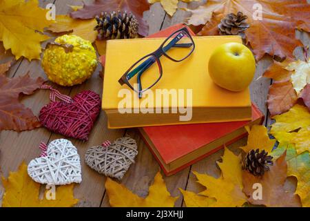 Herbsthintergrund. Alte Bücher, Apfel, Gläser und dekorative Herzen auf Holzplanken mit Herbstblättern. Design-Konzept für den Herbst. Stockfoto