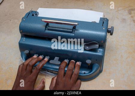 Nahaufnahme einer schwarzen blinden Person, die auf einem Braille-Drucker tippt Stockfoto