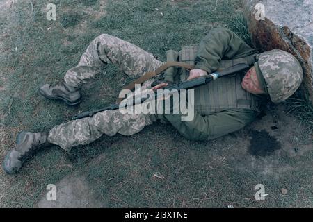 Ukrainischer verwundeter Soldat, der nach dem Kampf gegen den russischen Feind auf Gras in der Nähe des Felsens lag. Konzept der russischen militärischen Invasion in der Ukraine. Krieg in Großbritannien Stockfoto