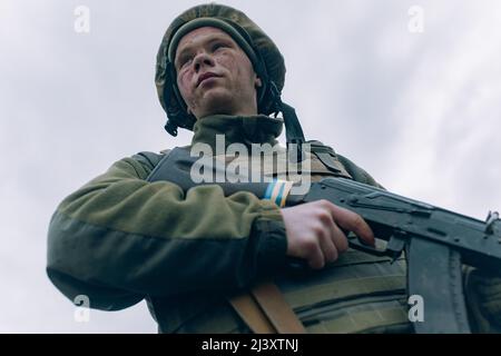 Porträt eines ukrainischen Soldaten im Helm mit kalaschnikow-Sturmgewehr vor Himmelshintergrund. Konzept der russischen militärischen Invasion in der Ukraine. War in Stockfoto