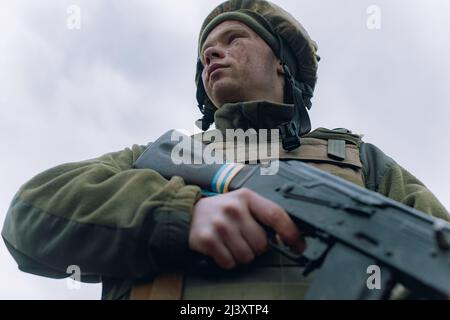 Porträt eines ukrainischen Soldaten im Helm mit kalaschnikow-Sturmgewehr vor Himmelshintergrund. Konzept der russischen militärischen Invasion in der Ukraine. War in Stockfoto