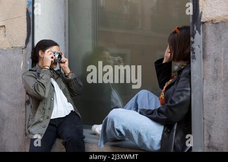 Gemischtes Mädchen, das ein Foto von einem anderen Mädchen auf der Straße fotografiert. Multiethnische Freunde, die Spaß haben. Stockfoto