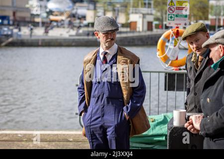 Mann, der am 9. April 2022 in Bristol Harbourside, Bristol, Großbritannien, in einem 1940s Jahre alten Hafenüberwachungskostüm mit Mosutache und flacher Mütze gekleidet war Stockfoto