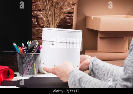 Frau Hände halten weißen Luxus runde Box. Frau arbeitet, Verpackung Artikel, Verpackung Geschenk auf dem Tisch. Freiberuflicher Arbeitsplatz, handgefertigtes Handwerk, Verkauf Stockfoto